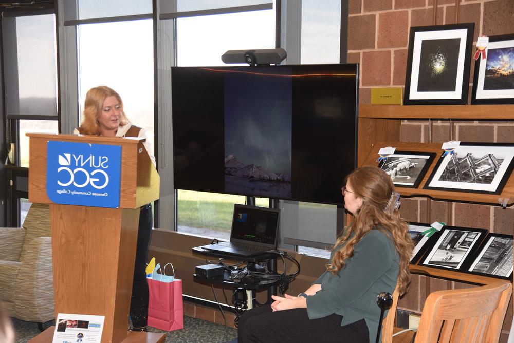 Assistant director of residence life Alicia O'Grady speaking at ceremony, slide showing her photography next to her